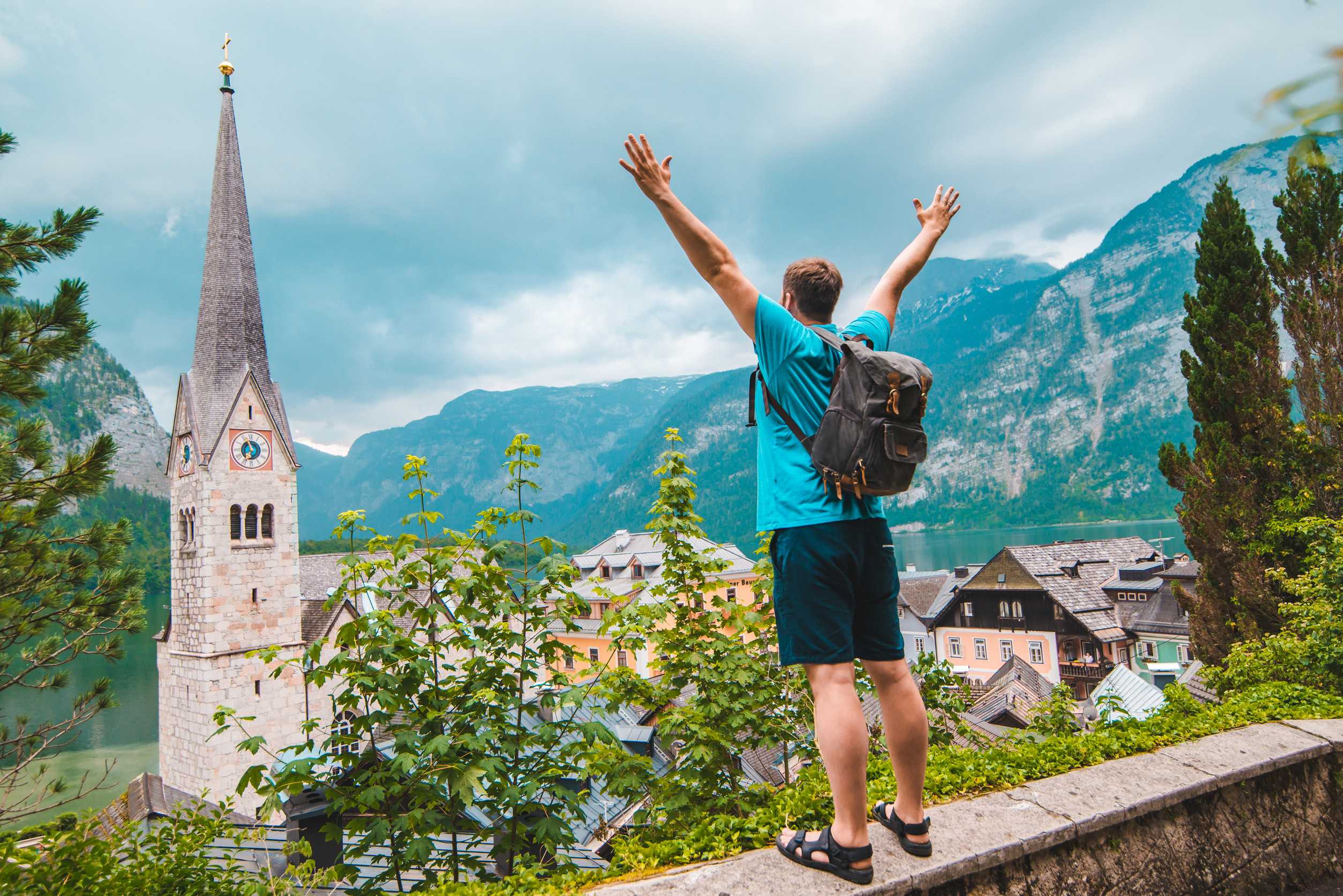 Happy Man Tourist Standing With Rising Up Hands Looking At Hallstatt City From Above Travel