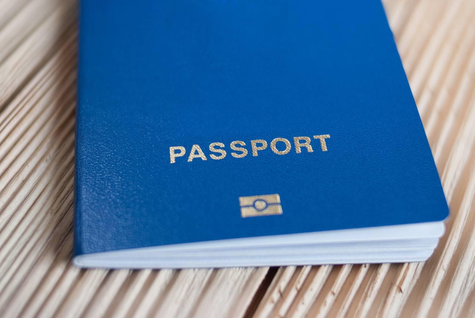 A blue passport with gold lettering placed on a wooden surface A blue passport with gold lettering placed on a wooden surface
